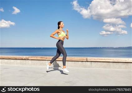 fitness, sport and healthy lifestyle concept - young woman running along sea promenade. young woman running along sea promenade