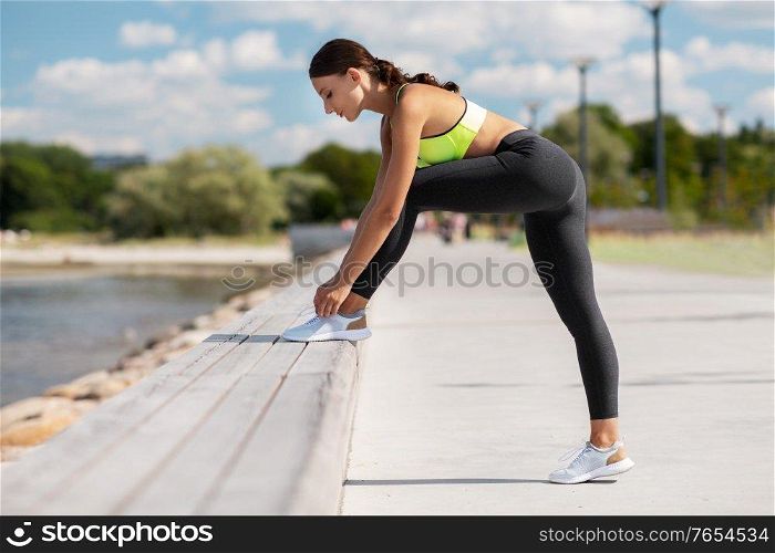 fitness, sport and healthy lifestyle concept - young woman tightening shoelaces on sneakers outdoors. sporty woman tightening shoelaces outdoors