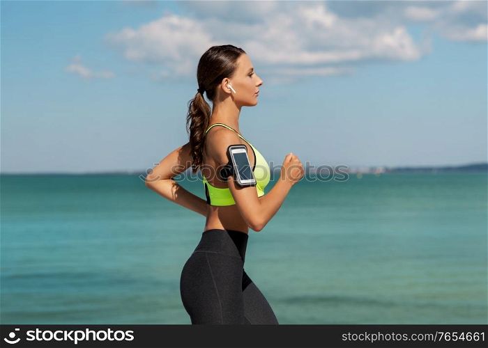 fitness, sport and healthy lifestyle concept - young woman with earphones and smartphone running outdoors. woman with earphones and smartphone running