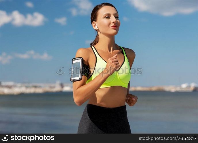 fitness, sport and healthy lifestyle concept - young woman with earphones and smartphone running outdoors. woman with earphones and smartphone running