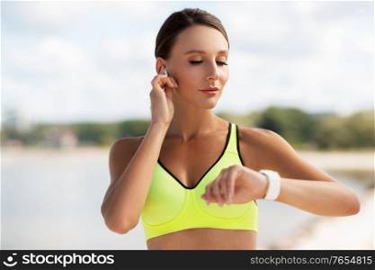 fitness, sport and healthy lifestyle concept - young woman with wireless earphones and smart watch exercising outdoors. woman with earphones and smart watch doing sports