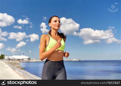 fitness, sport and healthy lifestyle concept - young woman with wireless earphones running along sea promenade. woman with wireless earphones running at seaside