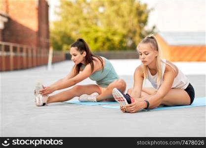 fitness, sport and healthy lifestyle concept - young women or female friends with activity trackers stretching outdoors. women with fitness trackers stretching outdoors