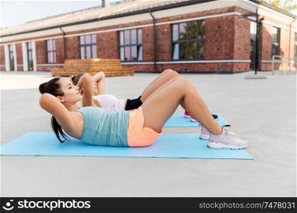 fitness, sport and healthy lifestyle concept - young women or female friends doing sit-ups on mat outdoors. women training and doing sit-ups outdoors