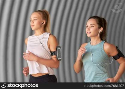 fitness, sport and healthy lifestyle concept - young women or female friends with earphones wearing armbands with smartphones and running outdoors. young women with earphones and smartphones running