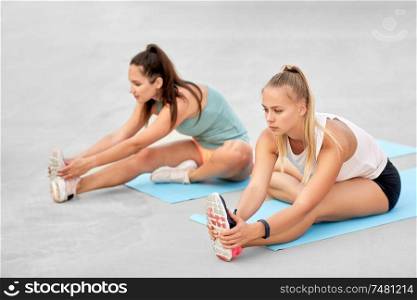 fitness, sport and healthy lifestyle concept - young women or female friends with activity trackers stretching outdoors. women with fitness trackers stretching outdoors