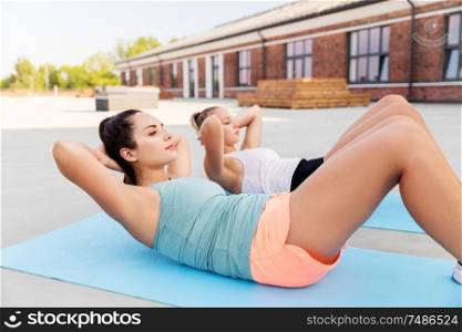fitness, sport and healthy lifestyle concept - young women or female friends doing sit-ups on mat outdoors. women training and doing sit-ups outdoors