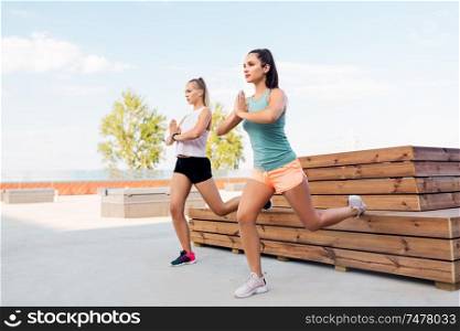 fitness, sport and healthy lifestyle concept - young women or female friends doing split squats outdoors. women training and doing split squats