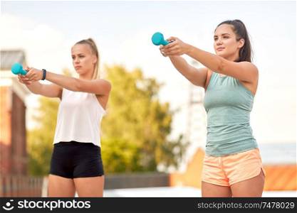 fitness, sport and healthy lifestyle concept - young women or female friends exercising with dumbbells outdoors. women exercising with dumbbells outdoors