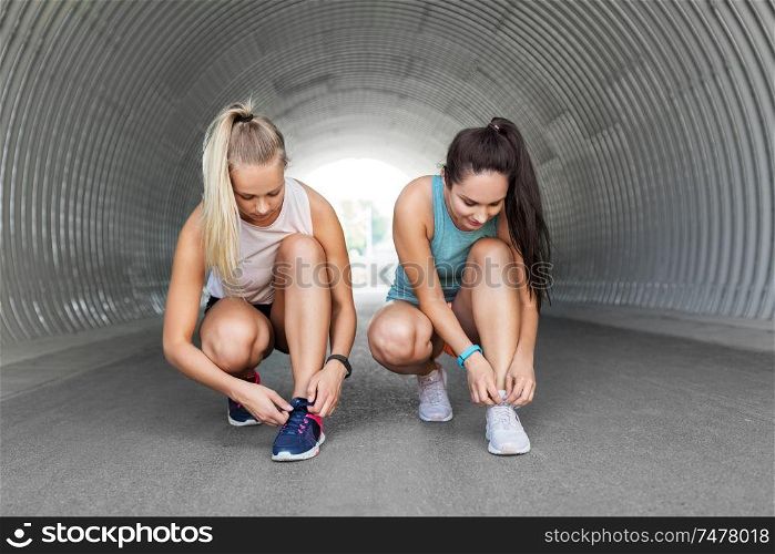 fitness, sport and healthy lifestyle concept - young women or female friends tying shoe laces outdoors. sporty women or female friends tying shoe laces