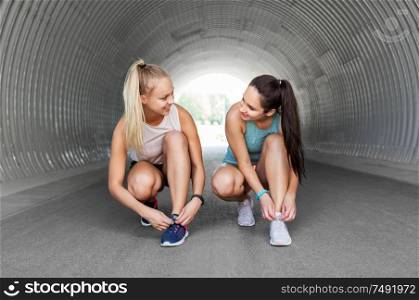 fitness, sport and healthy lifestyle concept - young women or female friends tying shoe laces outdoors. sporty women or female friends tying shoe laces