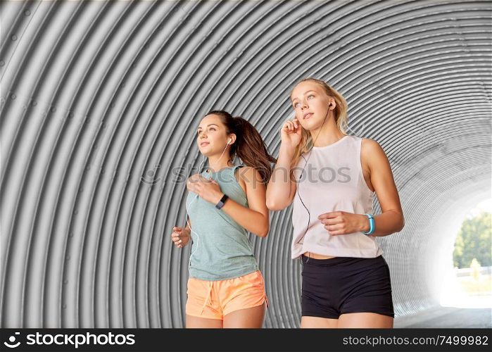 fitness, sport and healthy lifestyle concept - young women or female friends with earphones running outdoors. women or female friends with earphones running