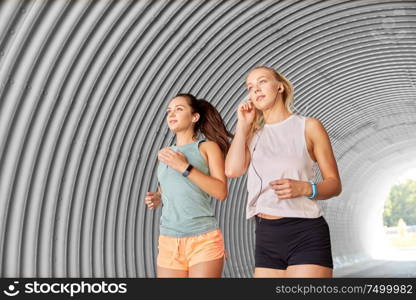 fitness, sport and healthy lifestyle concept - young women or female friends with earphones running outdoors. women or female friends with earphones running