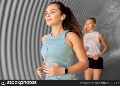 fitness, sport and healthy lifestyle concept - young women or female friends with earphones running outdoors. women or female friends with earphones running