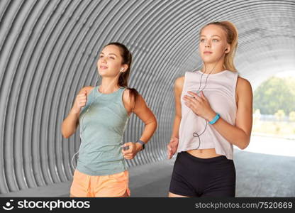 fitness, sport and healthy lifestyle concept - young women or female friends with earphones running outdoors. women or female friends with earphones running