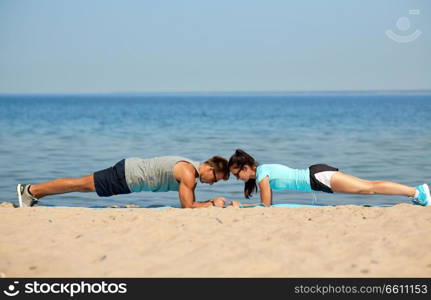 fitness, sport and lifestyle concept - couple doing plank exercise on summer beach. couple doing plank exercise on summer beach