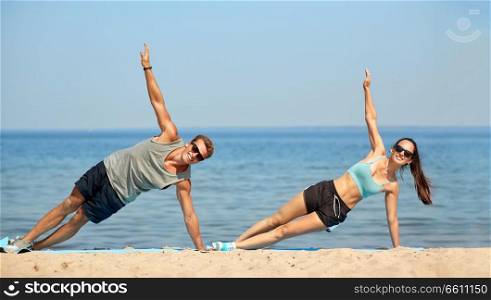 fitness, sport and lifestyle concept - couple doing side plank exercise on summer beach. couple doing side plank exercise on summer beach