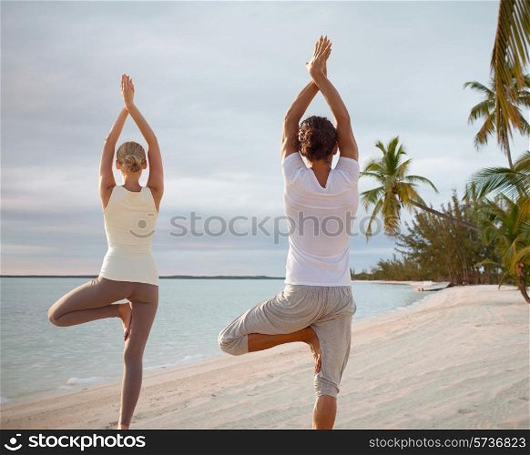 fitness, sport, and lifestyle concept - couple making yoga exercises on beach from back