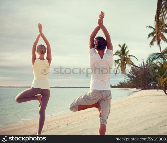 fitness, sport, and lifestyle concept - couple making yoga exercises on beach from back