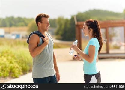 fitness, sport and lifestyle concept - couple with bottle of water talking after doing sports outdoors. couple with bottle of water after doing sports