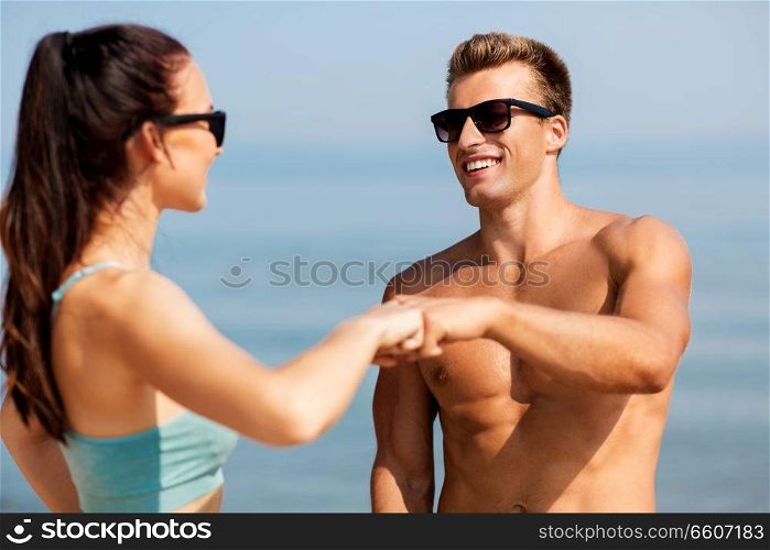 fitness, sport and lifestyle concept - happy couple in sports clothes and sunglasses on beach making fist bump gesture. happy couple in sports clothes and shades on beach