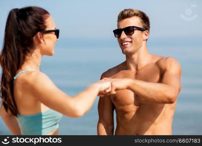 fitness, sport and lifestyle concept - happy couple in sports clothes and sunglasses on beach making fist bump gesture. happy couple in sports clothes and shades on beach