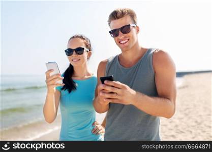 fitness, sport and lifestyle concept - happy couple in sports clothes and sunglasses with smartphones on beach. couple in sports clothes with smartphones on beach
