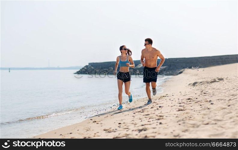 fitness, sport and lifestyle concept - happy couple in sports clothes and sunglasses running along summer beach. couple in sports clothes running along on beach