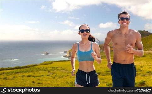 fitness, sport and lifestyle concept - happy couple in sports clothes and sunglasses running over big sur hills background in california. couple in sports clothes running along on beach