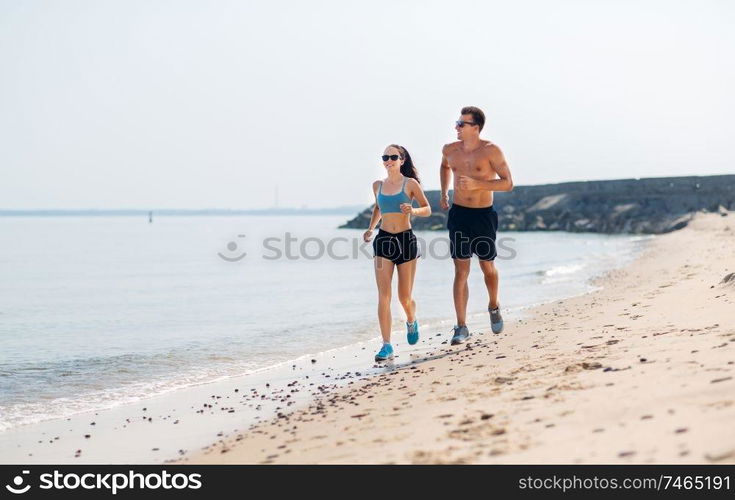 fitness, sport and lifestyle concept - happy couple in sports clothes and sunglasses running along summer beach. couple in sports clothes running along on beach