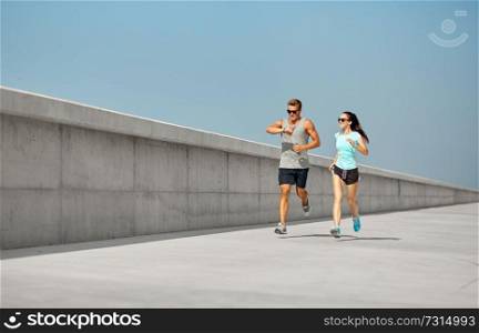 fitness, sport and lifestyle concept - happy couple in sports clothes and sunglasses running outdoors. couple in sports clothes running outdoors