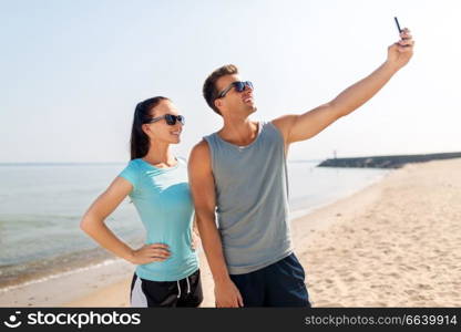 fitness, sport and lifestyle concept - happy couple in sports clothes taking selfie by smartphone on beach. couple taking selfie by smartphone on beach