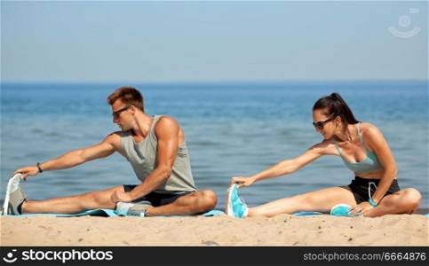 fitness, sport and lifestyle concept - happy couple stretching legs on beach before training. happy couple stretching legs on beach