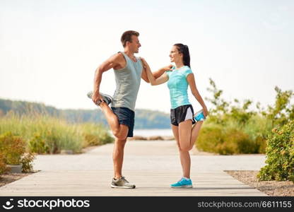 fitness, sport and lifestyle concept - smiling couple stretching legs on beach before training. smiling couple stretching legs on beach