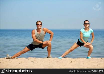 fitness, sport and lifestyle concept - smiling couple stretching legs on beach before training. smiling couple stretching legs on beach