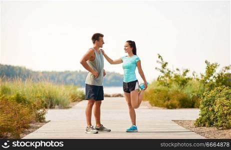 fitness, sport and lifestyle concept - smiling couple stretching legs on beach before training. smiling couple stretching legs on beach