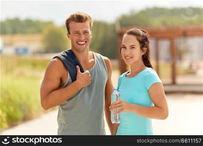 fitness, sport and lifestyle concept - smiling couple with towel and bottle of water after doing sports. couple with bottle of water after doing sports