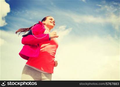 fitness, sport and lifestyle concept - smiling young woman with earphones running outdoors