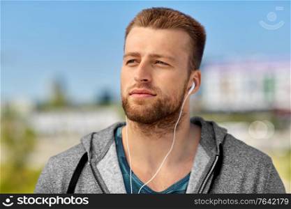 fitness, sport and lifestyle concept - young man in earphones listening to music outdoors. man in earphones listening to music outdoors