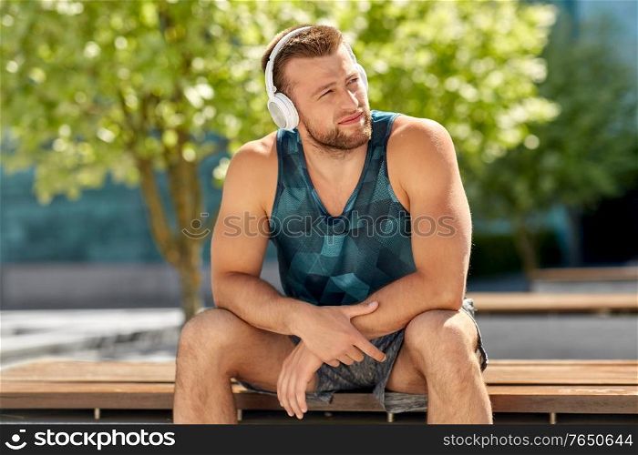 fitness, sport and lifestyle concept - young man in headphones listening to music sitting on city street. man in headphones listening to music outdoors