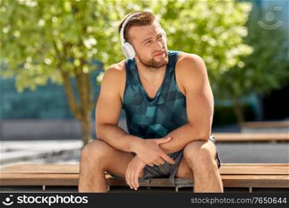 fitness, sport and lifestyle concept - young man in headphones listening to music sitting on city street. man in headphones listening to music outdoors