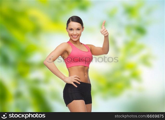 fitness, sport and people concept - beautiful athletic woman in sportswear showing thumbs up over green natural background. sporty woman in sportswear showing thumbs up. sporty woman in sportswear showing thumbs up