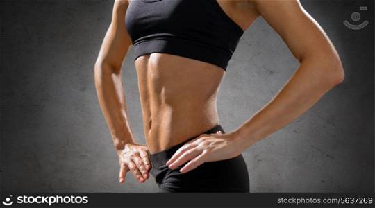 fitness, sport and people concept - close up of beautiful athletic female abs in sportswear over concrete wall background