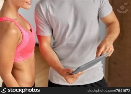 fitness, sport and people concept - close up of young woman and personal trainer with tablet pc computer in gym. close up of man and woman with tablet pc in gym
