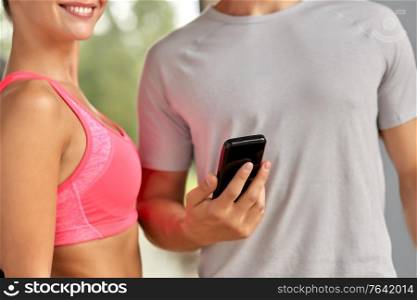 fitness, sport and people concept - close up of young woman and personal trainer with smartphone in gym. close up of man and woman with smartphone in gym