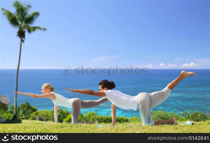fitness, sport and people concept - couple making yoga balancing table pose outdoors over exotic natural background with palm tree and ocean. couple making yoga balancing table pose outdoors