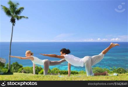 fitness, sport and people concept - couple making yoga balancing table pose outdoors over exotic natural background with palm tree and ocean. couple making yoga balancing table pose outdoors