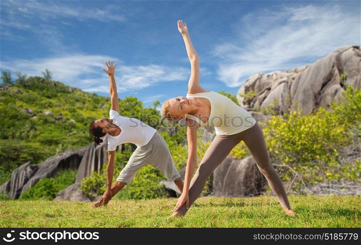 fitness, sport and people concept - happy couple doing yoga outdoors over natural background. happy couple doing yoga outdoors