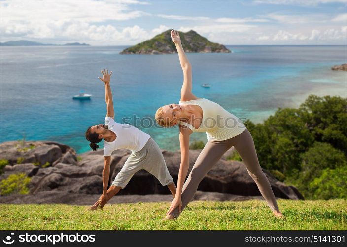 fitness, sport and people concept - happy couple doing yoga outdoors over natural background and sea. happy couple doing yoga outdoors