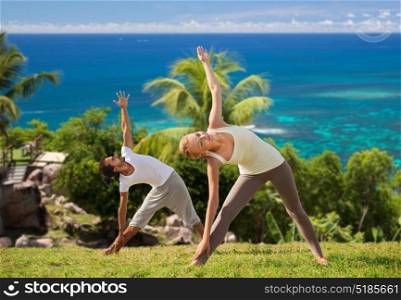 fitness, sport and people concept - happy couple doing yoga outdoors over natural background and sea. happy couple doing yoga outdoors